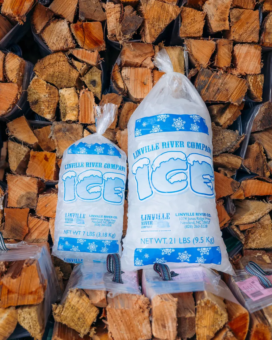 Two bags of Linville River Company ice resting against a wall of split kiln-dried firewood