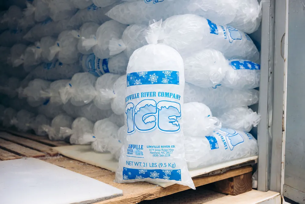 A 21 lb bag of Linville River Company ice in front of stacked bags in cold storage